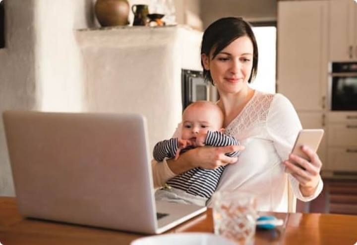 Avdantages of using a mortgage broker | Mum with a baby sitting at a kitchen table with her phone and a laptop