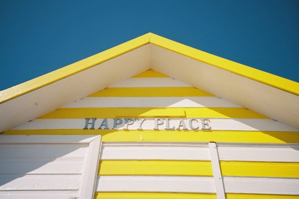 Best places to live | A Beach hut with striped yellow panels and a sign saying "Happy Place"