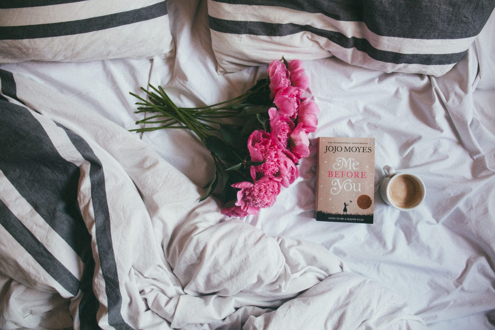 Buy-to-Let Secured Loans | A bunch of pink flowers and a book on an unmade bed with black and white striped sheets