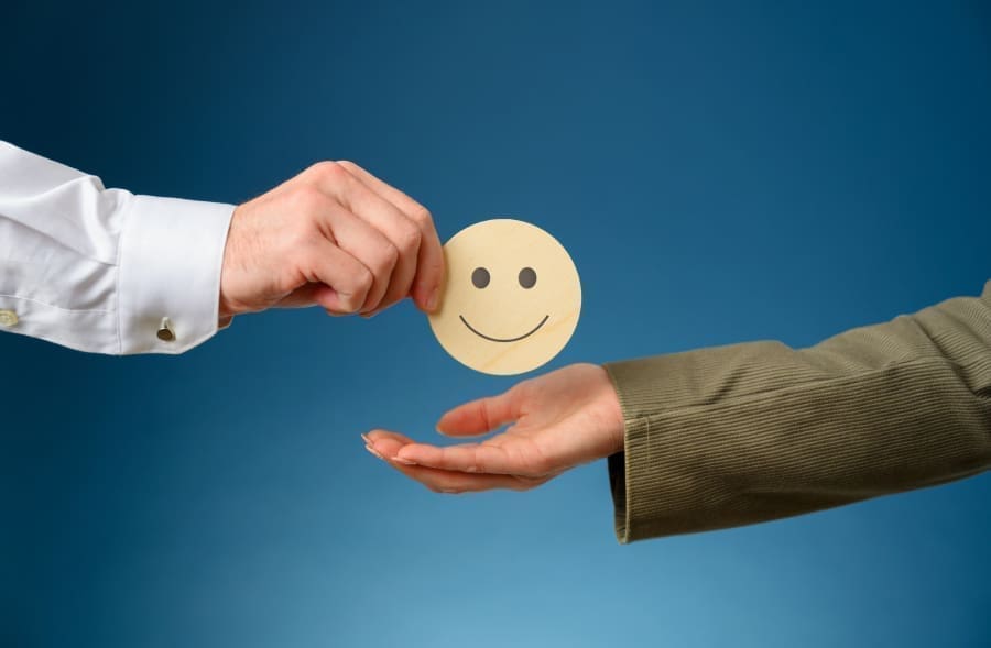 Customer Service | One hand passing a paper smiley face to another hand on a blue background