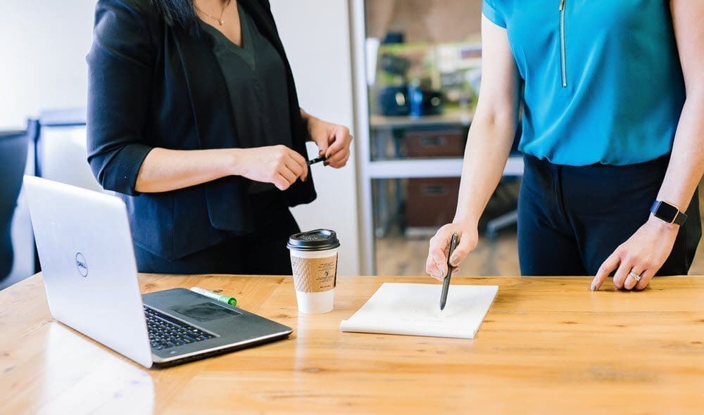 Mortgage Prisoners | Two people standing next to a desk with a coffee and a laptop, discussing paperwork