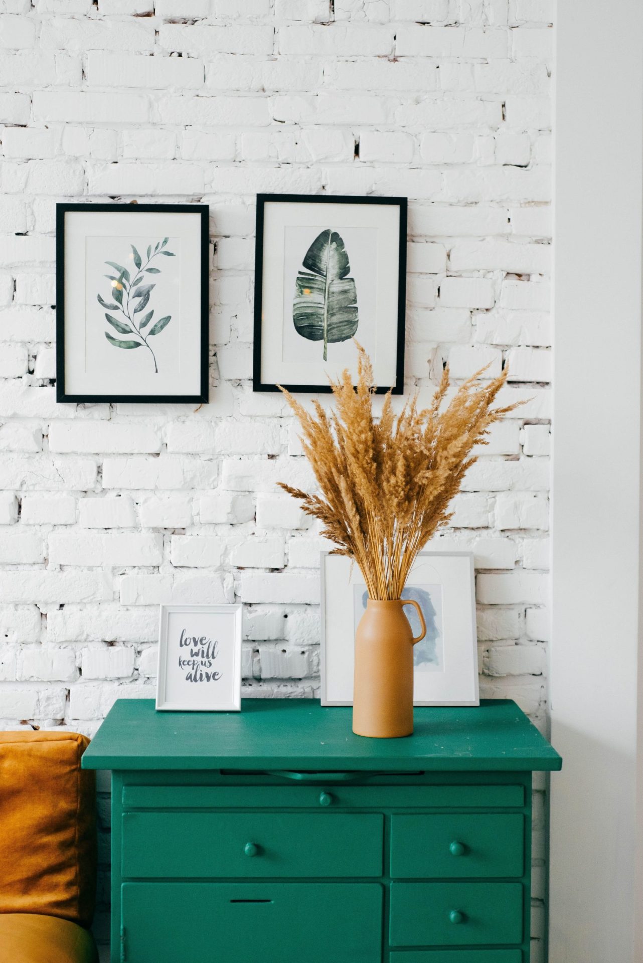 Remortgage for Home Improvements | Image of a green chest of draws with pampas grass in a vase and artiwork in the background and on the white brick wall