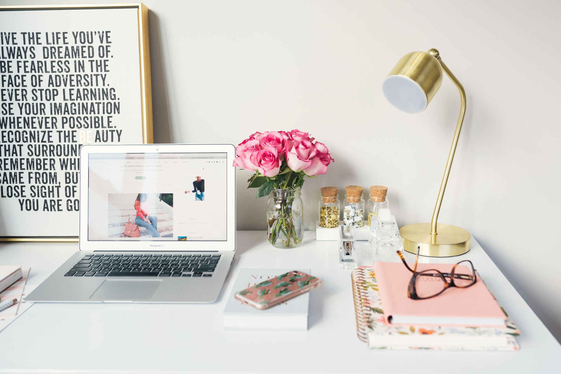 White desk with a laptop, flowers, lamp and books on it