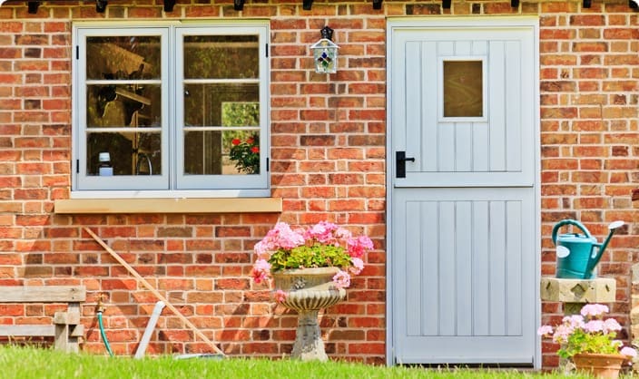 Widget Mortgages | Country house pale blue door with red brick surroundings, green grass, a watering can and flowers