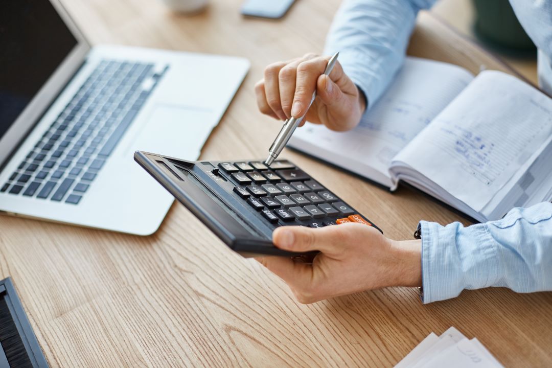 a person using a calculator at a desk with a laptop on it