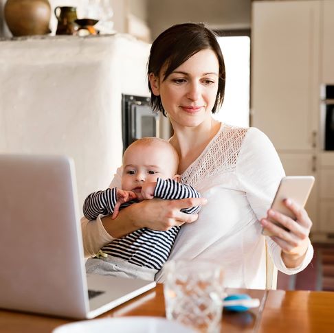 Mortgage Brokers covering the UK | Mum with a baby sitting at a kitchen table with her phone and a laptop